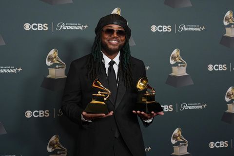 Musiker Leon Thomas hält zwei Grammys in den Händen und lächelt in die Kamera