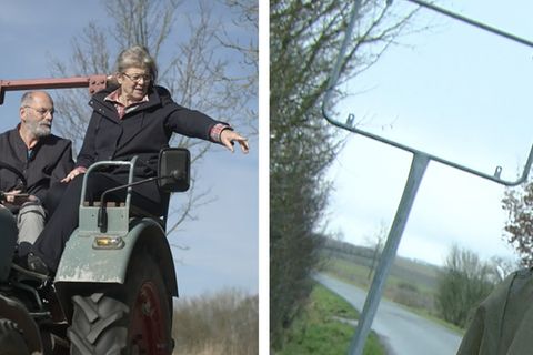 Ein Bürgermeister mit seiner Frau auf einem Traktor. Auf der rechten Seite ein leerer Ortsschild -Rahmen.