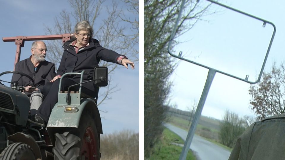 Ein Bürgermeister mit seiner Frau auf einem Traktor. Auf der rechten Seite ein leerer Ortsschild -Rahmen.