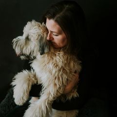 Frau umarmt weissen flauschigen Hund vor schwarzem Hintergrund