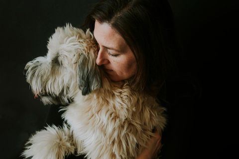 Frau umarmt weissen flauschigen Hund vor schwarzem Hintergrund