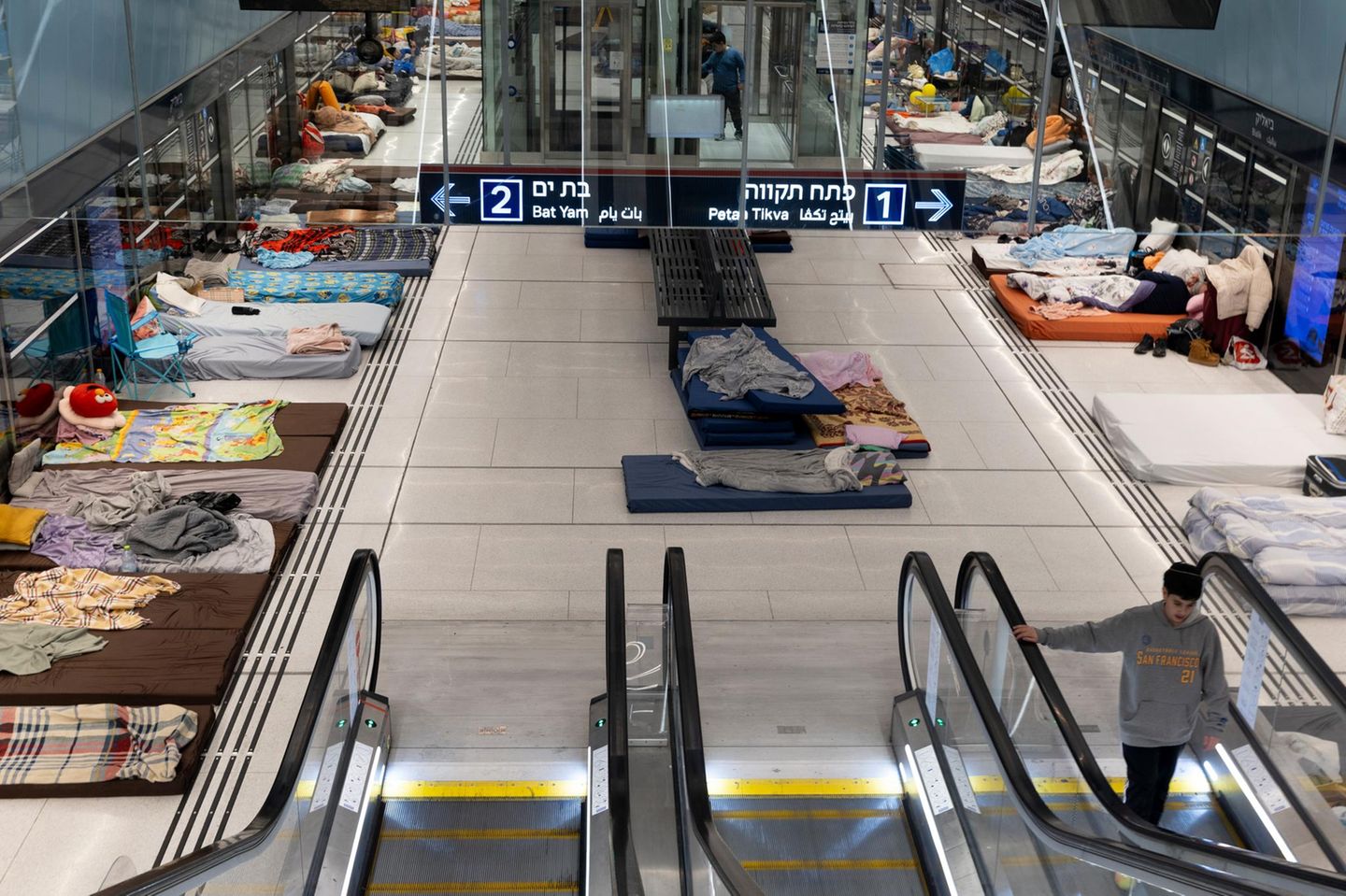 Matratzen, Kissen und Decken liegen an den Rändern der Bahnstation. Von oben ist die Rolltreppe und die Halle zu sehen.