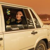 Junge Frau sitzt im Auto und schaut aus dem Fenster.