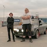 Zwei Jungs stehen mit verschrenkten Armen vor einem grauen Auto (Toyota)