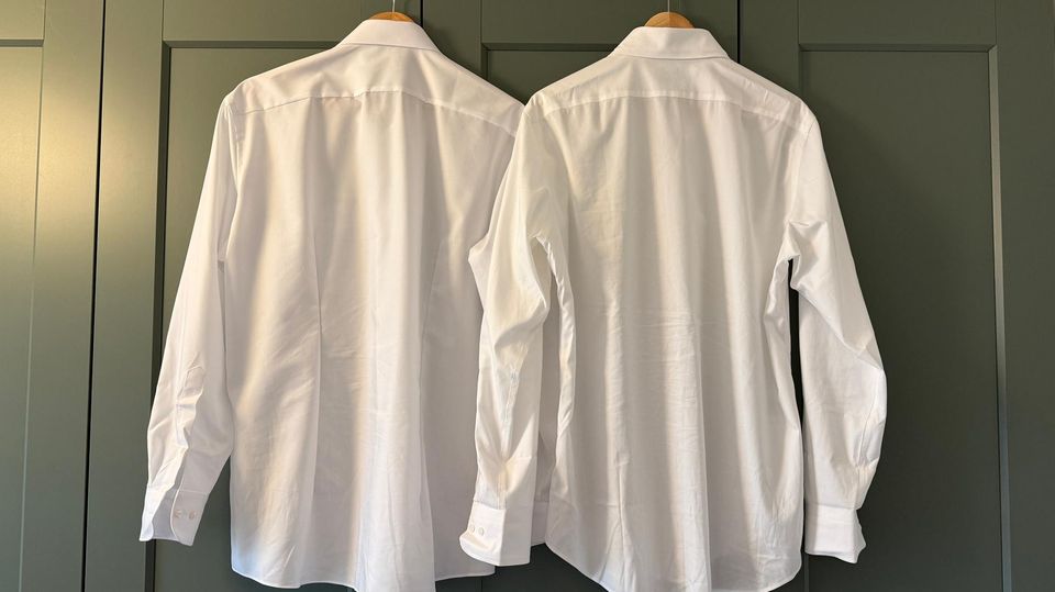 Olymp- und Uniqlo-Hemd hängen vor einer grünen Schrankwand