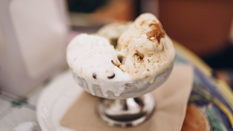 Aus einem silbernen Eisbecher quillt beigefarbenes Milcheis