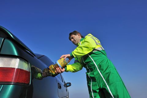 Ein Mann tankt Sonnenblumenöl aus einer Plastikflasche in ein Auto.