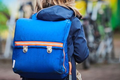 Ein Schüler steht mit Schulranzen nahe einer Grundschule.