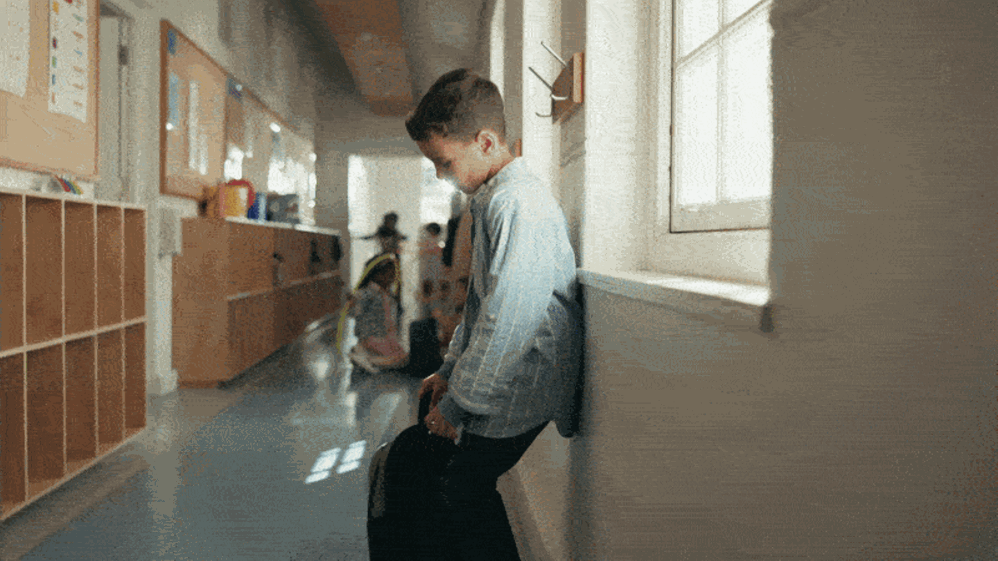 Kinder - Ein kleiner Junge sackt an einer Wand in der Schule zusammen und vergräbt seinen Kopf zwischen seinen Armen