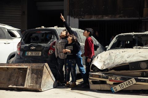 Kinder stehen zwischen zerstörten Autos und zeigen in den Himmel