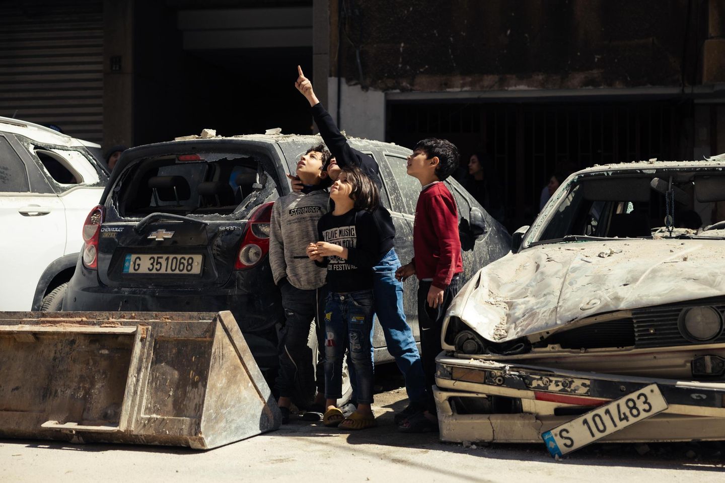 Kinder stehen zwischen zerstörten Autos und zeigen in den Himmel
