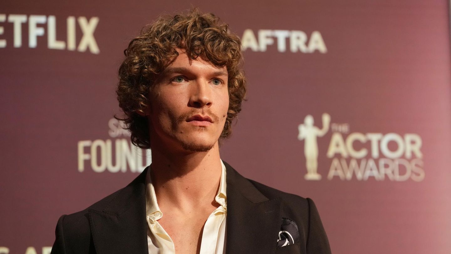 Connor Storrie posiert vor einer Fotowand mit ernstem Gesichtsausdruck