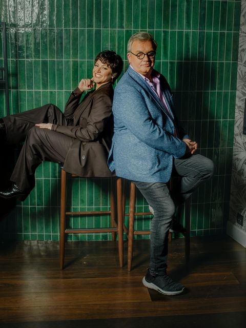 Hape Kerkeling und Tahnee sitzen Rücken an Rücken auf Barhockern vor einer grün gefließten Wand