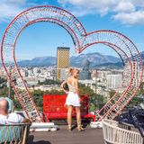 Eine Frau posiert vor einem Herzrahmen, im Hintergrund die Stadt Tirana