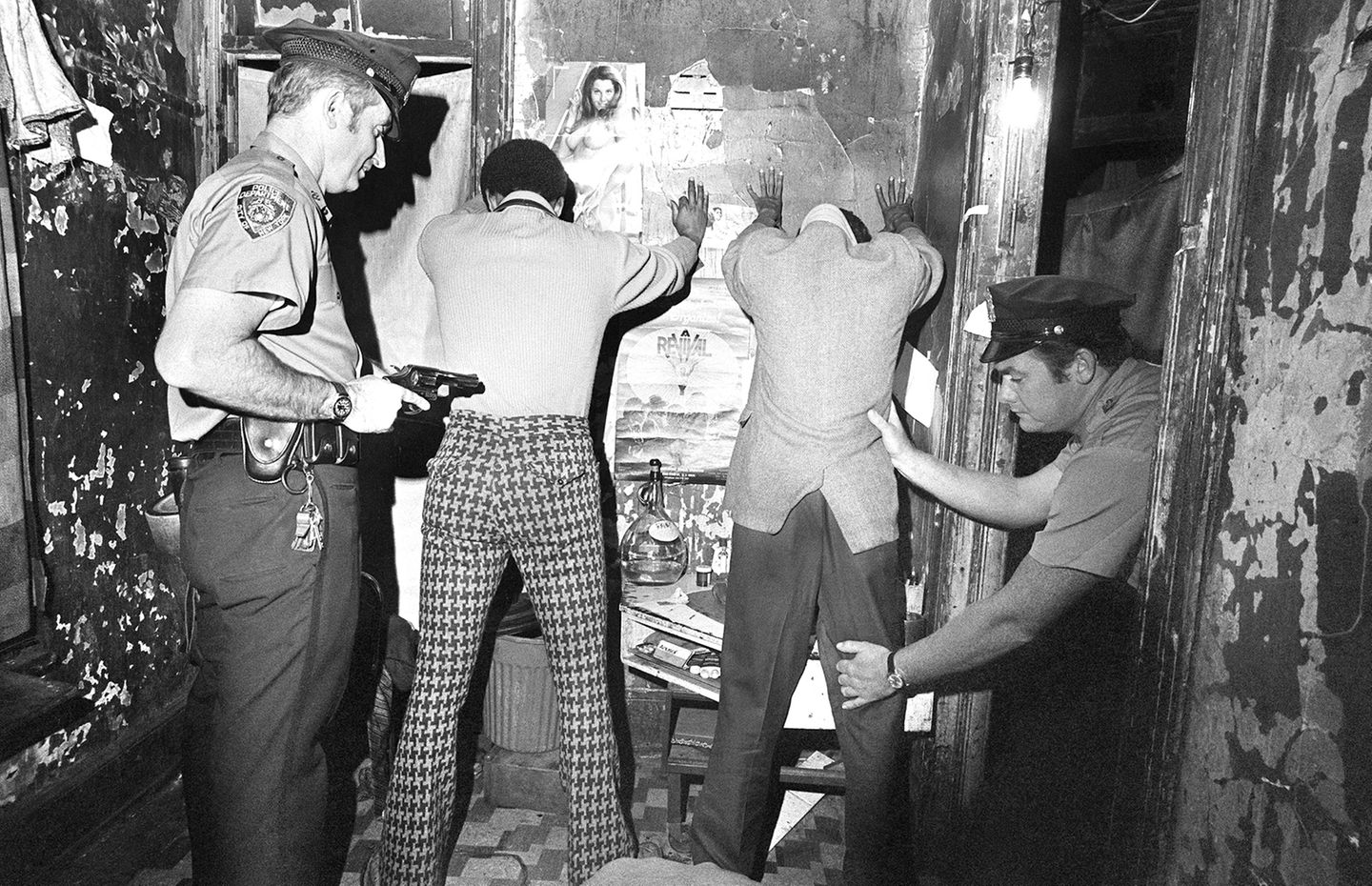 Zwei Polizisten durchsuchen zwei Männer, die an einer Wand stehen