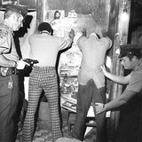 Zwei Polizisten durchsuchen zwei Männer, die an einer Wand stehen