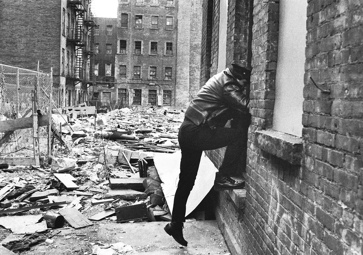 Ein Polizist klettert in ein Fenster eines abbruchreifen Hauses