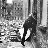 Ein Polizist klettert in ein Fenster eines abbruchreifen Hauses