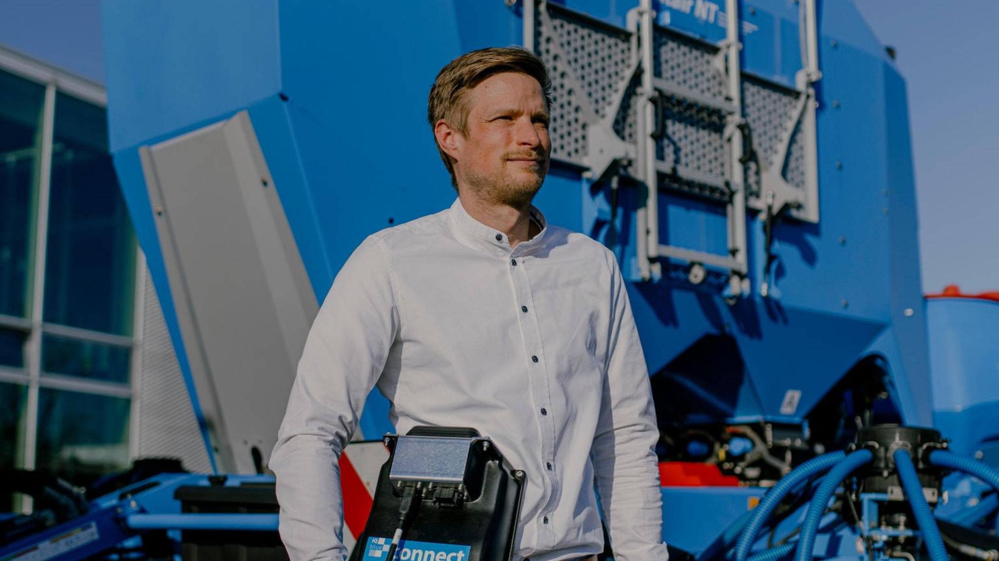 Ein Mann aus dem Mittelstand steht vor einer blauen Landmaschine in der Sonne