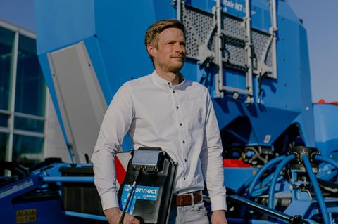 Ein Mann aus dem Mittelstand steht vor einer blauen Landmaschine in der Sonne