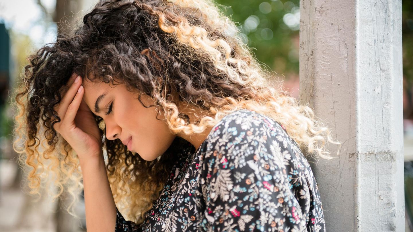 Frau mit Migräne lehnt an Pfeiler