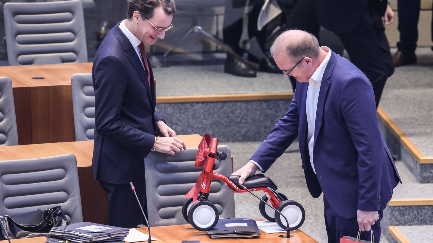 Jochen Ott (SPD, r.) überreicht Hendrik Wüst (CDU) das 1. FC-Köln-Laufrad im Plenarsaal des Landtags. Foto: Oliver Berg/dpa