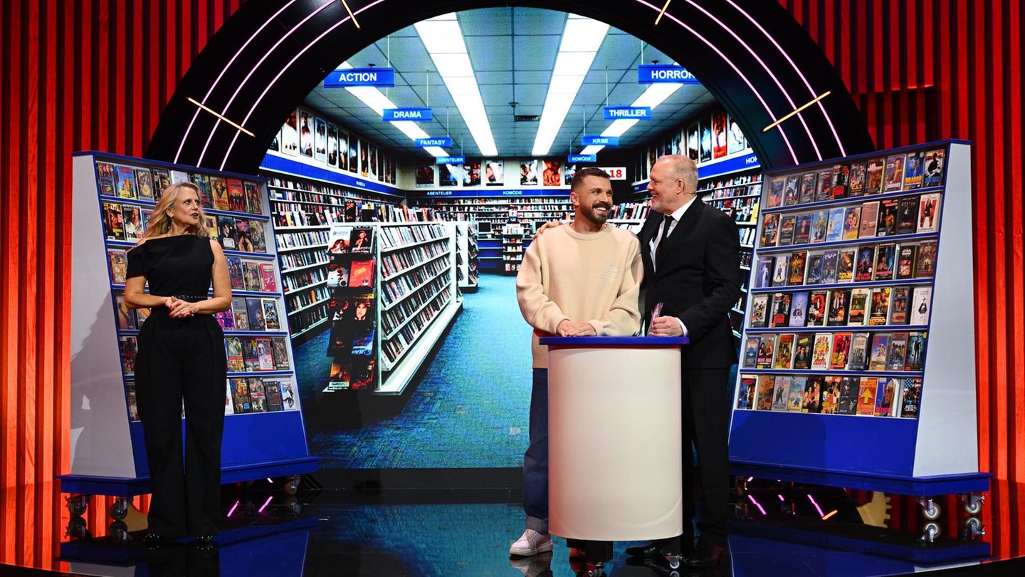 Edin Hasanovi steht mit Barbara Schöneberger und Stefan Raab vor der Kulisse einer Videothek