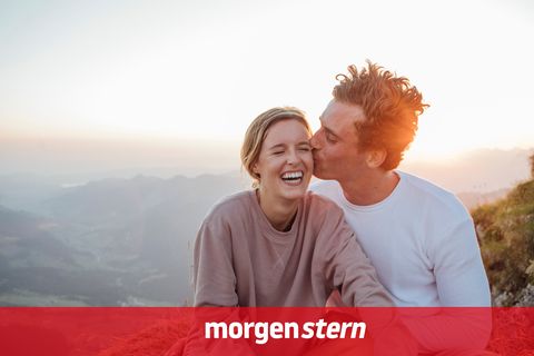 Glücklicher Mann küsst in den Bergen eine Frau, im Hintergrund öffnet sich der Blick ins Tal