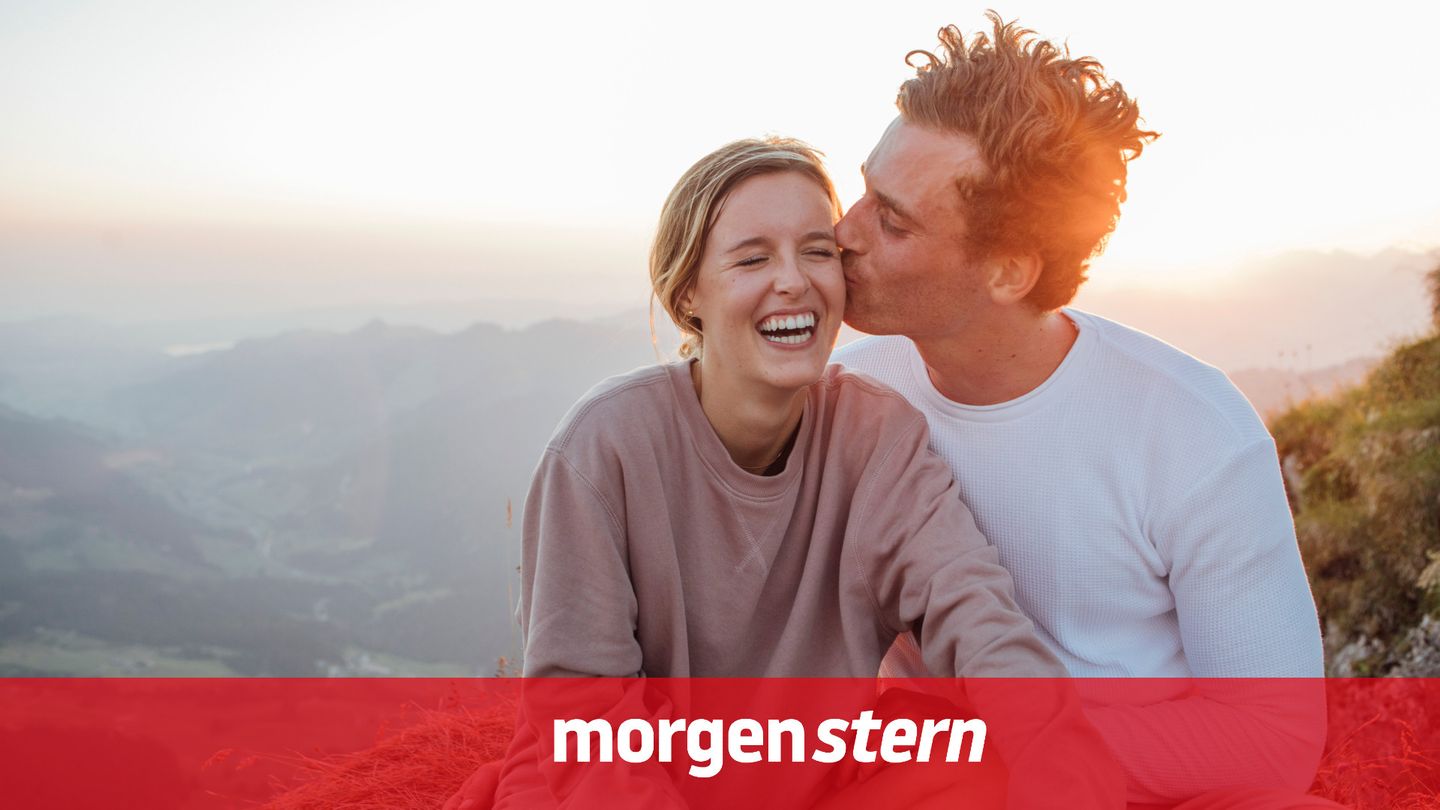 Glücklicher Mann küsst in den Bergen eine Frau, im Hintergrund öffnet sich der Blick ins Tal