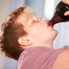 Zuckersteuer: Ein übergewichtiger Junge trinkt Cola aus einer Flasche