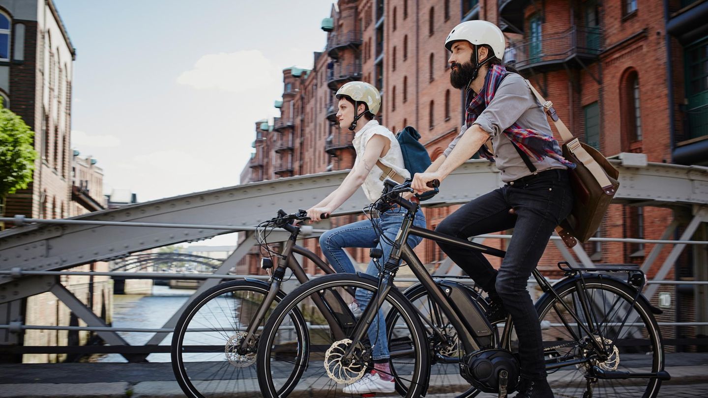 Zwei Personen fahren auf E-Bikes durch die Hamburger Speicherstadt. Beide tragen einen Helm
