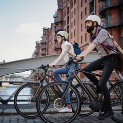 Zwei Personen fahren auf E-Bikes durch die Hamburger Speicherstadt. Beide tragen einen Helm