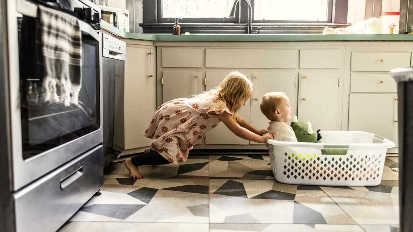 Kind schiebt geschwister im Wäschekorb durch die Küche