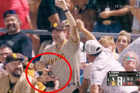 Ein Baseball-Fan fängt einen Ball mit einem schlafenden Baby auf dem Arm.