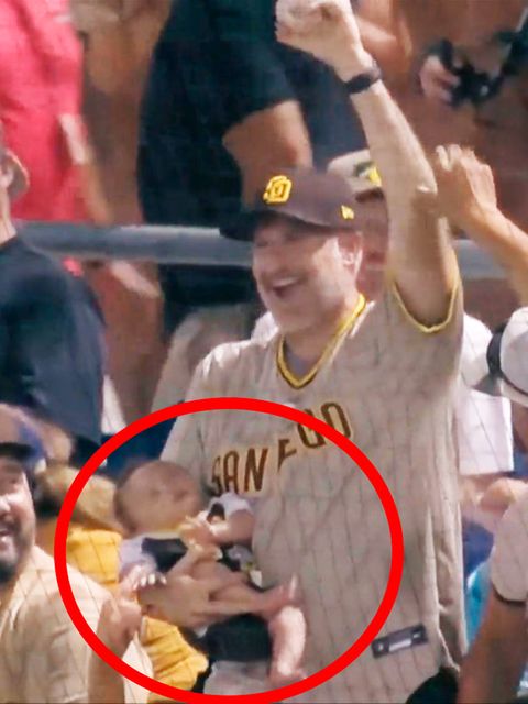 Ein Baseball-Fan fängt einen Ball mit einem schlafenden Baby auf dem Arm.