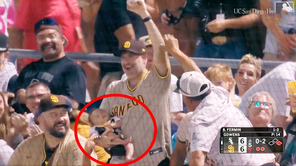 Ein Baseball-Fan fängt einen Ball mit einem schlafenden Baby auf dem Arm.