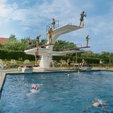 Personen springen von einem Sprungturm im Freibad