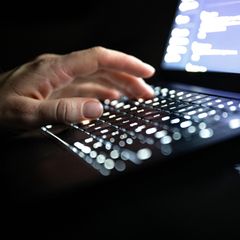 Eine linke Männerhand tippt auf der Tastatur eines Laptops – Symbolbid für Cyberangriffe