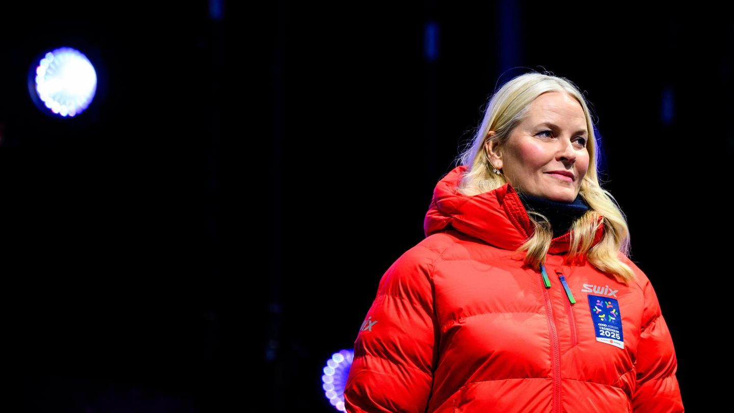 Mette-Marit trägt eine orangefarbene Jacke und lächelt in die Ferne