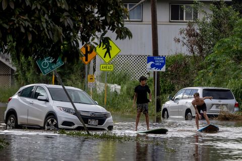 Hochwasser in Hawaii: Zwei Jugendliche surfen in Waialua neben einem liegengebliebenen Fahrzeug