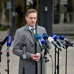 Premier Golob spricht nach der Slowenien-Wahl in grauem Mantel auf der Straße in eine Reihe vor ihm aufgebauter Mikros