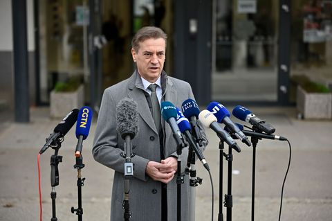 Premier Golob spricht nach der Slowenien-Wahl in grauem Mantel auf der Straße in eine Reihe vor ihm aufgebauter Mikros