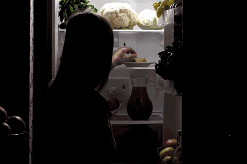 Eine Frau isst im dunkeln eine Eiswaffel aus dem Kühlschrank, Essstörung