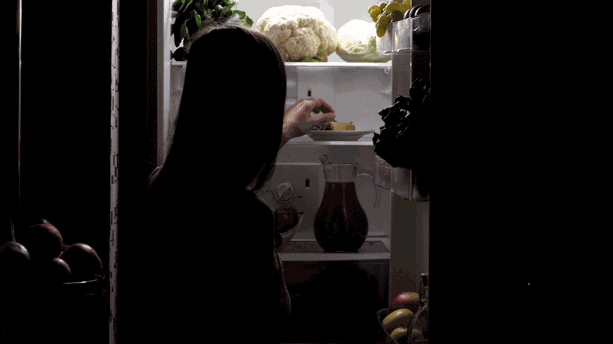 Eine Frau isst im dunkeln eine Eiswaffel aus dem Kühlschrank, Essstörung