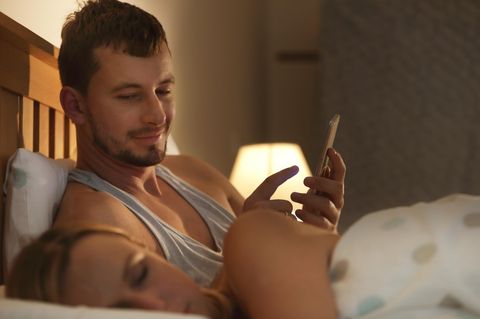 Ein Paar liegt im Bett, die Frau schläft und der Mann ist am Handy und schaut auf die Frau