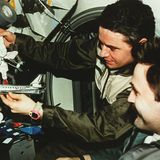 Zwei Kosmonauten halten Papiermodelle vom Shuttle Atlantis und der Raumstation Mir in der Hand