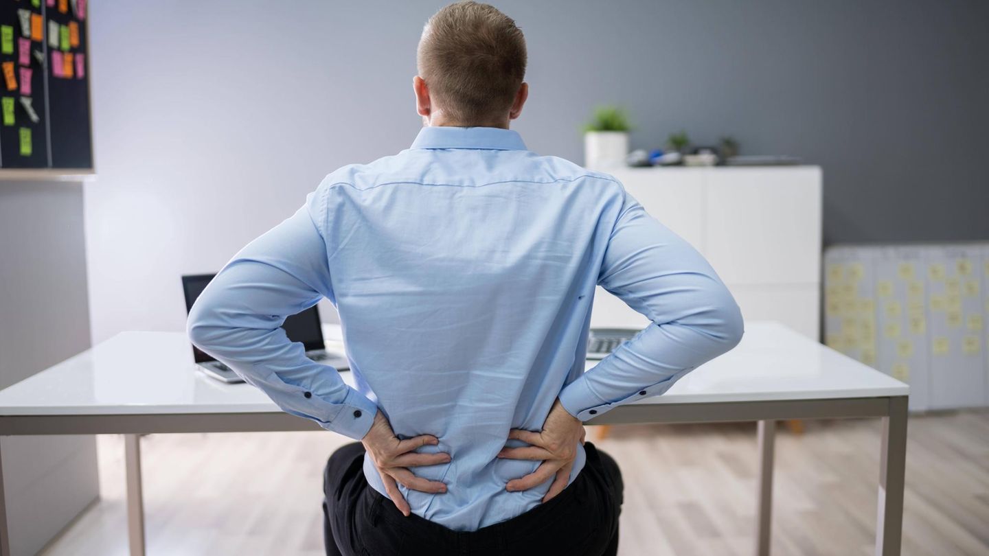 Ein Mann sitzt auf einem Hocker und fasst sich an den Rücken (Symbolbild Rente)