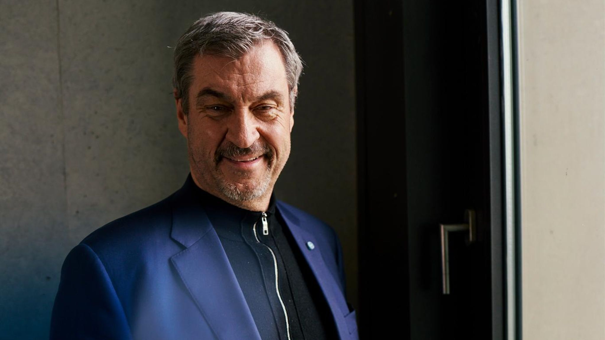Markus Söder schaut in die Kamera, hinter einer Scheibe sieht man den CSU-Schriftzug