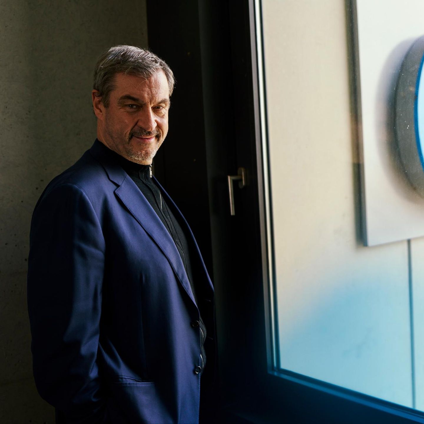 Markus Söder schaut in die Kamera, hinter einer Scheibe sieht man den CSU-Schriftzug