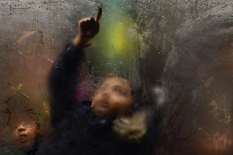 Kind im Bus zeichnet mit dem Finger auf beschlagene Scheibe